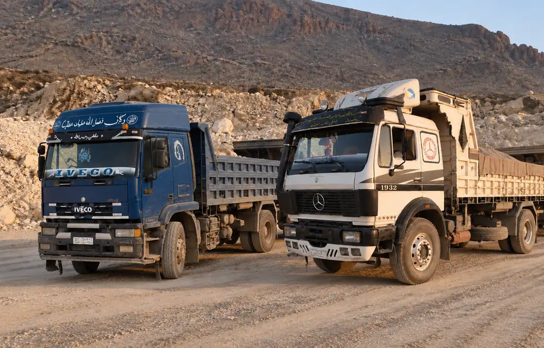 Two dump trucks from the Sapex fleet, a blue Iveco and a white Mercedes with a trailer, parked in the quarry yard