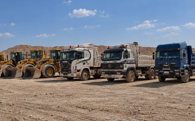 A row of dump trucks and loaders lined up in the quarry yard