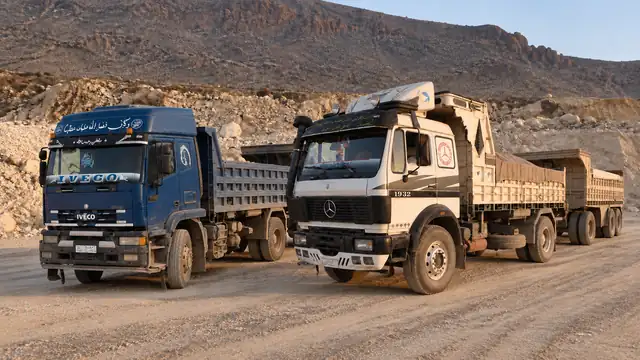 Two dump trucks with trailers, a blue Iveco and a white Mercedes, side by side in the quarry yard