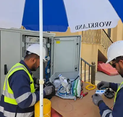 Two technicians splicing fiber optic cable inside an outdoor distribution cabinet under a canopy
